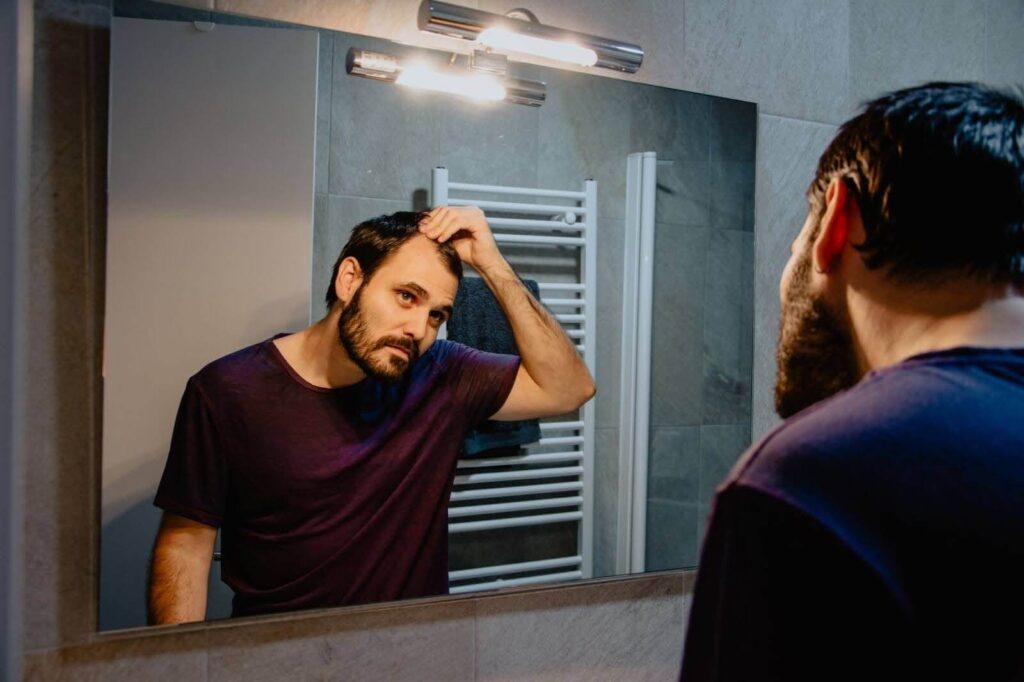 A man feeling and looking at his hair in the mirror.